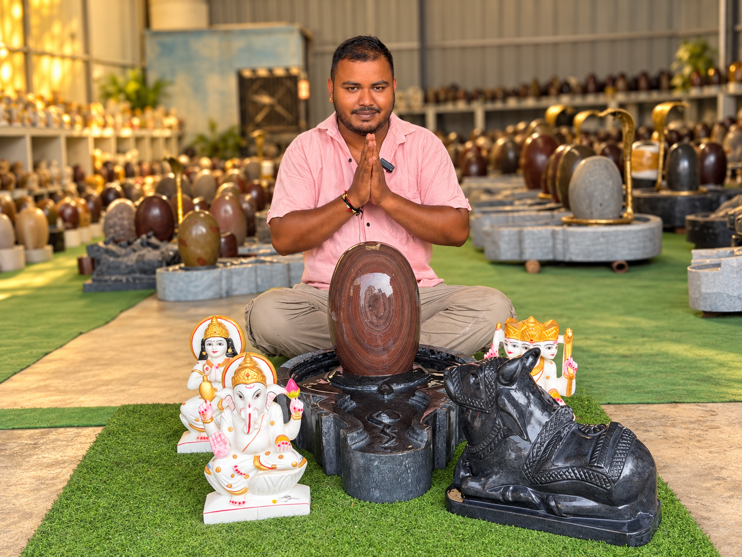 A man offering namaste behind a Narmadeshwar Shivling in a Shivling workshop